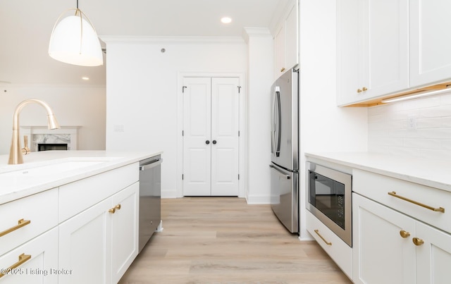 kitchen featuring decorative backsplash, stainless steel appliances, crown molding, white cabinetry, and a sink