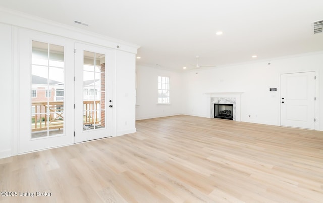 unfurnished living room featuring light wood finished floors, a premium fireplace, visible vents, and ornamental molding