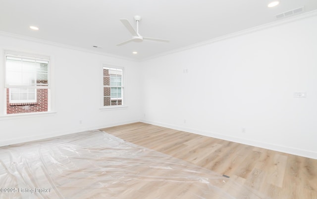 spare room featuring ornamental molding, visible vents, light wood-style flooring, and baseboards