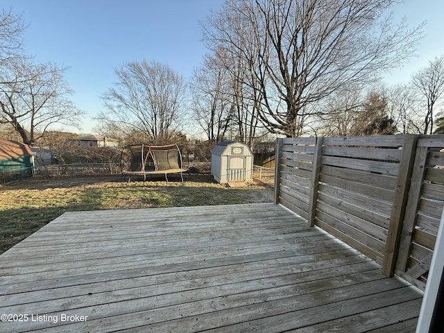 wooden terrace with a trampoline, an outbuilding, a fenced backyard, and a shed