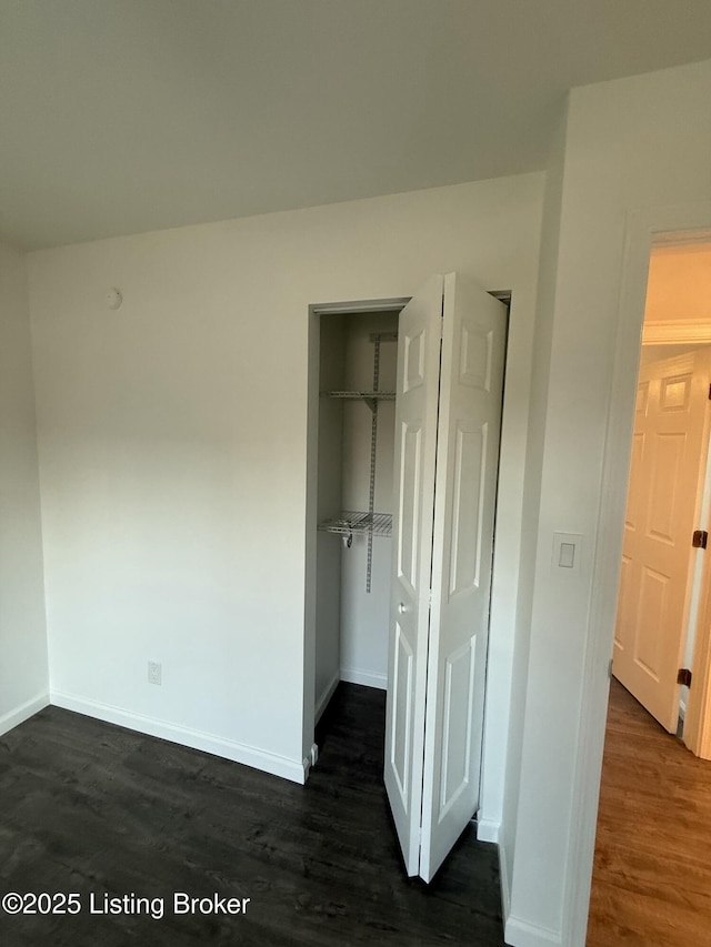 unfurnished bedroom with a spacious closet, a closet, baseboards, and dark wood-type flooring