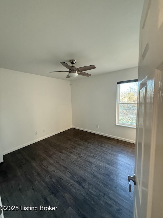 spare room with dark wood-type flooring, a ceiling fan, and baseboards