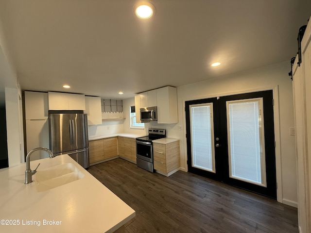 kitchen featuring a barn door, dark wood finished floors, stainless steel appliances, french doors, and a sink