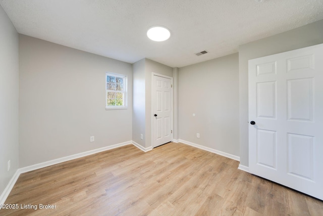 unfurnished bedroom featuring a textured ceiling, light wood-type flooring, visible vents, and baseboards