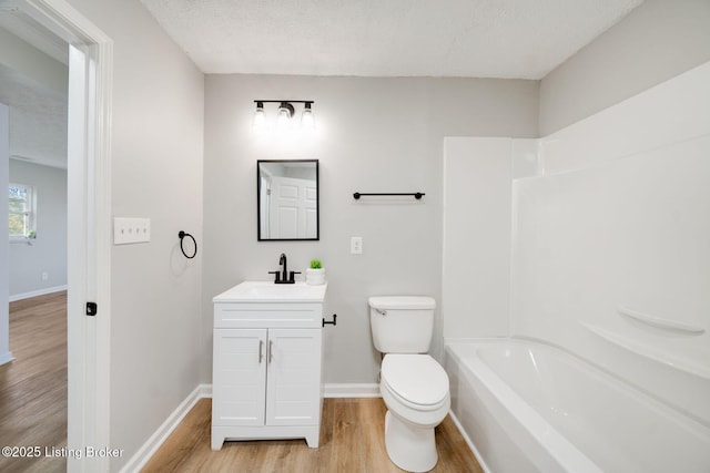 full bathroom with wood finished floors, a textured ceiling, toilet, and vanity