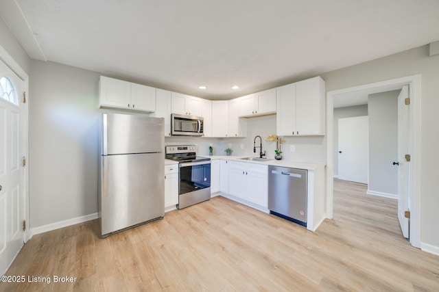 kitchen with white cabinets, appliances with stainless steel finishes, baseboards, and a sink