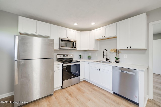 kitchen with a sink, light wood-style floors, stainless steel appliances, white cabinetry, and recessed lighting