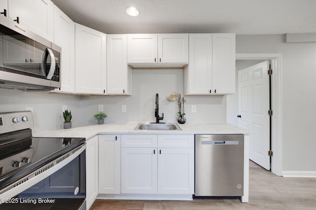 kitchen with white cabinets, light countertops, a sink, light wood-style flooring, and appliances with stainless steel finishes