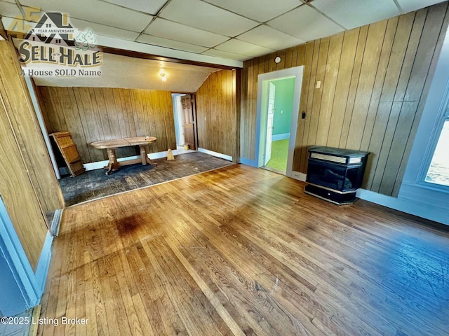 unfurnished living room featuring baseboards, a drop ceiling, wood finished floors, and wooden walls