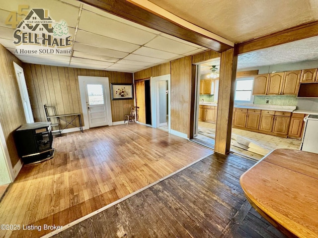 living room featuring a wood stove, light wood-style floors, wooden walls, and baseboards