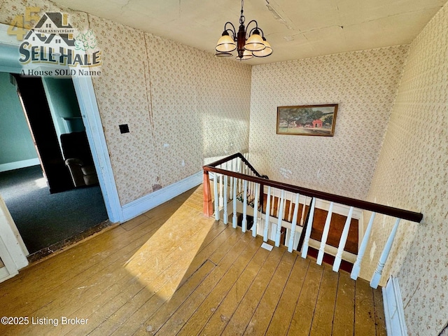 stairs with baseboards, wood-type flooring, an inviting chandelier, and wallpapered walls