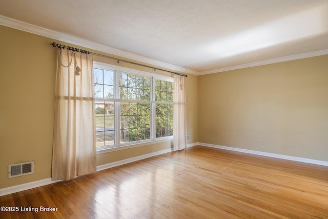 spare room with crown molding, wood finished floors, visible vents, and baseboards