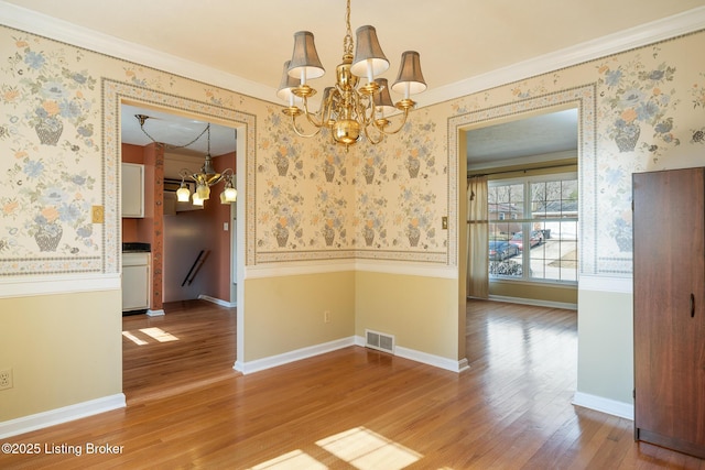 unfurnished dining area with an inviting chandelier, wood finished floors, visible vents, and wallpapered walls