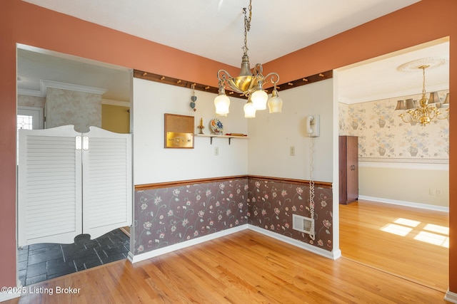 unfurnished dining area featuring a wainscoted wall, visible vents, wood finished floors, a chandelier, and wallpapered walls