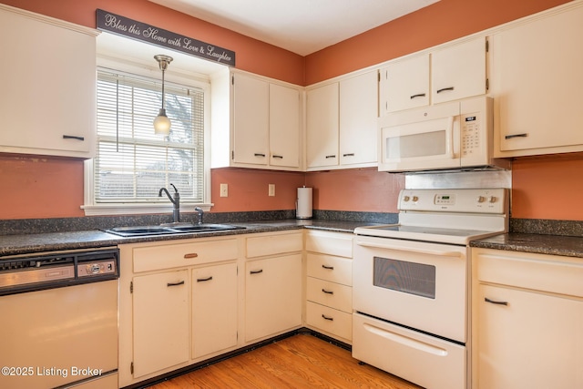 kitchen featuring white appliances, dark countertops, light wood-type flooring, pendant lighting, and a sink