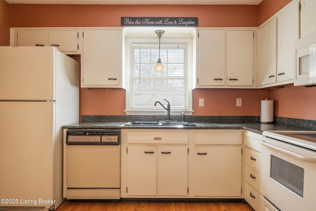 kitchen featuring white appliances, dark countertops, light wood-type flooring, pendant lighting, and a sink