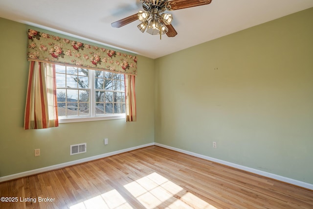 spare room with a ceiling fan, wood finished floors, visible vents, and baseboards