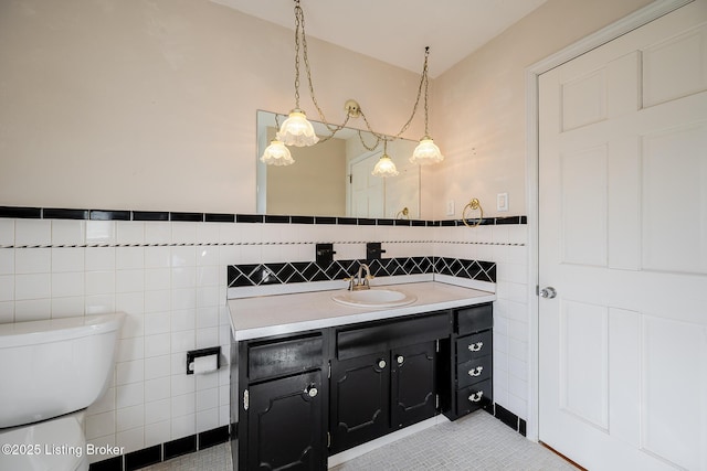 bathroom with tile walls, toilet, wainscoting, vanity, and tile patterned floors