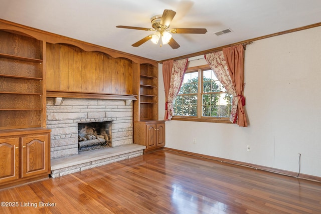 unfurnished living room featuring baseboards, visible vents, a ceiling fan, wood finished floors, and a stone fireplace