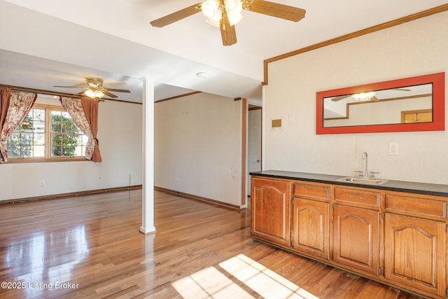 kitchen featuring light wood finished floors, brown cabinetry, dark countertops, ornamental molding, and a sink