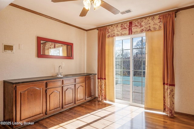 doorway with visible vents, ceiling fan, wood finished floors, crown molding, and a sink