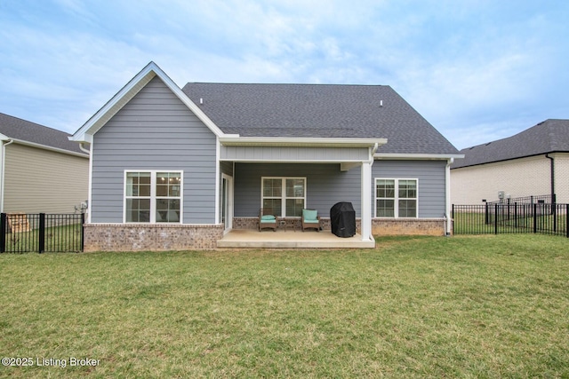 back of property with brick siding, a shingled roof, a fenced backyard, a yard, and a patio area