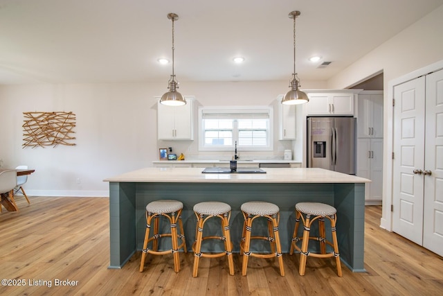 kitchen featuring visible vents, stainless steel fridge with ice dispenser, light countertops, white cabinets, and a center island