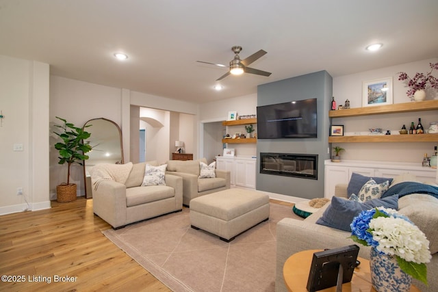 living area featuring a ceiling fan, recessed lighting, arched walkways, light wood-style floors, and a glass covered fireplace