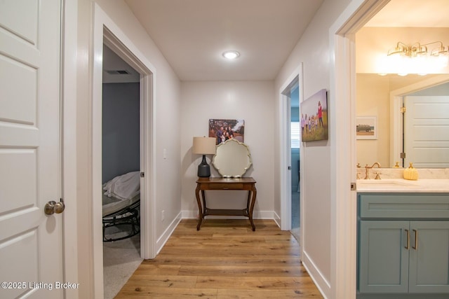 corridor with visible vents, baseboards, light wood-type flooring, and a sink