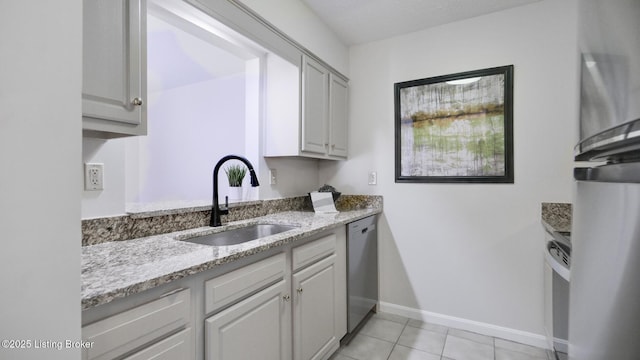 kitchen featuring light tile patterned floors, a sink, baseboards, stainless steel dishwasher, and light stone countertops