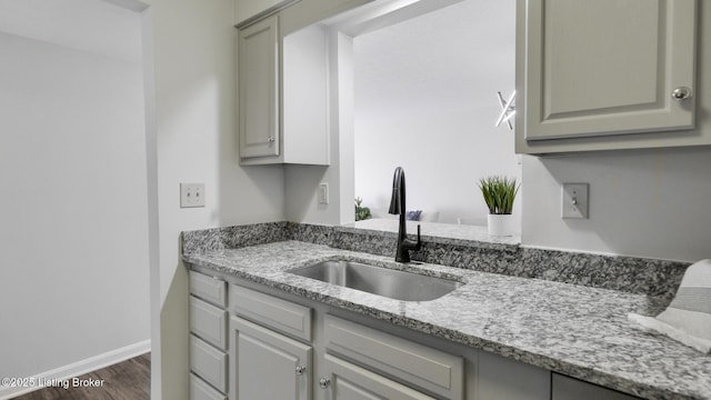 kitchen with baseboards, light stone counters, dark wood-type flooring, gray cabinets, and a sink