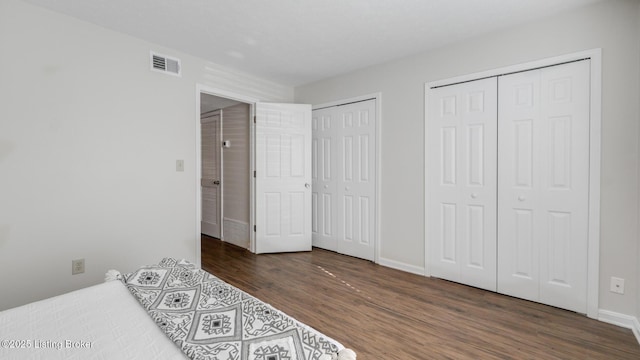 bedroom featuring baseboards, visible vents, multiple closets, and wood finished floors