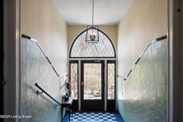 foyer featuring a towering ceiling, plenty of natural light, tile walls, and a notable chandelier