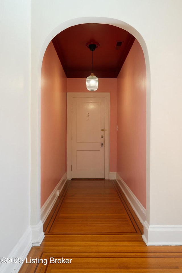 hallway with light wood-type flooring, visible vents, arched walkways, and baseboards