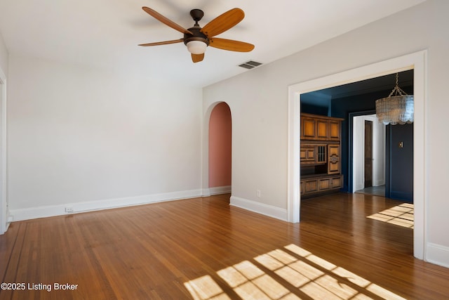 spare room with arched walkways, ceiling fan, wood finished floors, visible vents, and baseboards