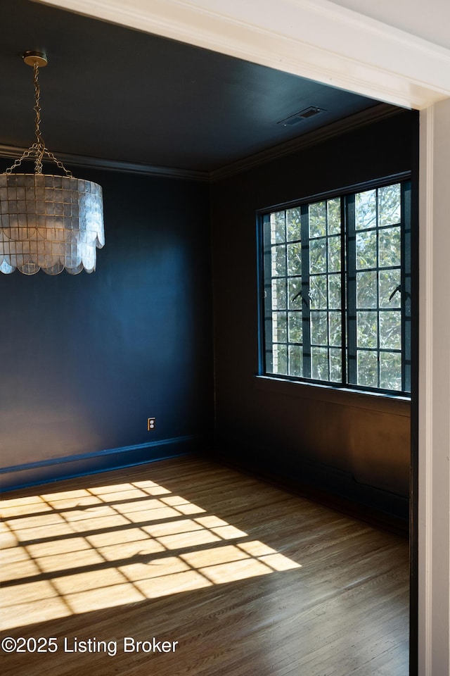 empty room with ornamental molding, visible vents, baseboards, and wood finished floors