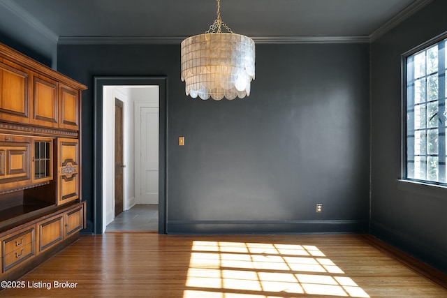 unfurnished dining area with baseboards, a chandelier, wood finished floors, and crown molding