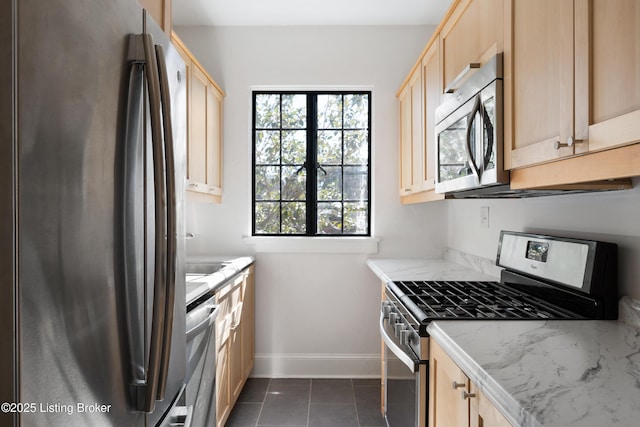 kitchen with stainless steel appliances, light brown cabinetry, dark tile patterned floors, and light stone counters