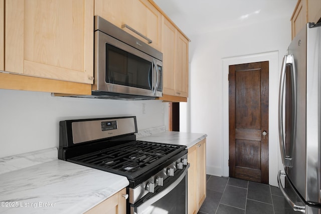 kitchen with stainless steel appliances, dark tile patterned floors, light stone counters, and light brown cabinetry