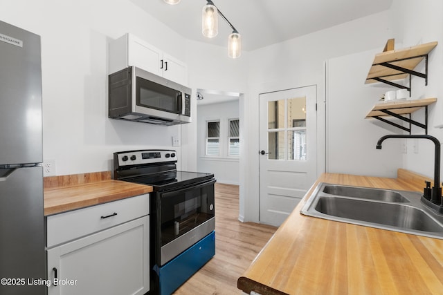 kitchen featuring white cabinets, wood counters, appliances with stainless steel finishes, light wood-type flooring, and a sink