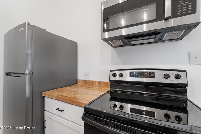 kitchen with stainless steel appliances, wooden counters, and white cabinetry