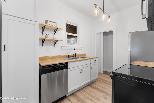 kitchen with light wood finished floors, butcher block countertops, stainless steel appliances, white cabinetry, and a sink