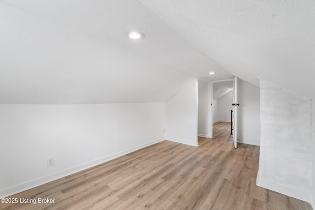 additional living space featuring vaulted ceiling, light wood-type flooring, and baseboards