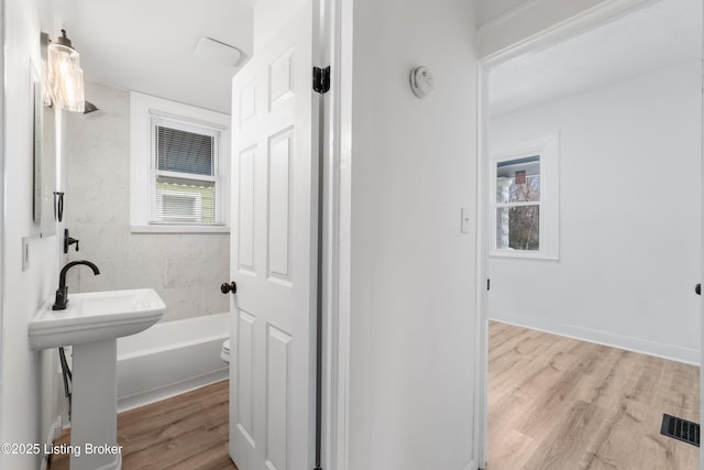 bathroom featuring visible vents, a sink, a bathing tub, and wood finished floors