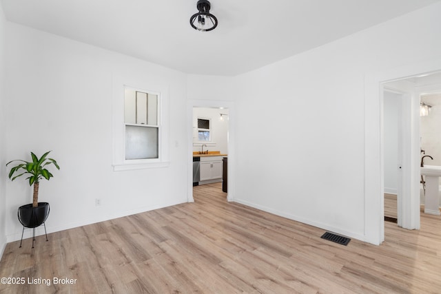 unfurnished room featuring visible vents, a sink, light wood-style flooring, and baseboards