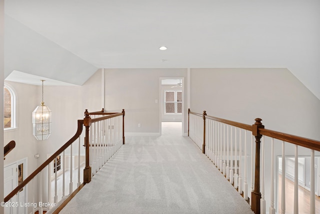 hall featuring light colored carpet, lofted ceiling, an upstairs landing, a chandelier, and a wealth of natural light