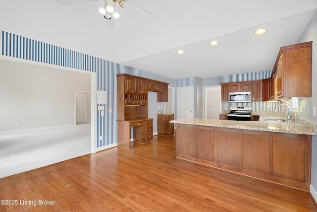 kitchen with light wood finished floors, a peninsula, light stone countertops, stainless steel appliances, and a sink