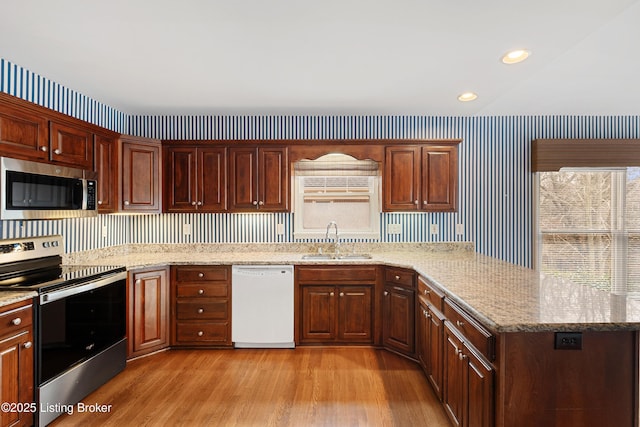 kitchen featuring wallpapered walls, stainless steel appliances, a sink, and light wood finished floors