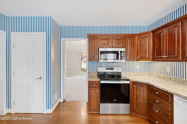 kitchen featuring appliances with stainless steel finishes, light wood finished floors, light stone counters, and wallpapered walls