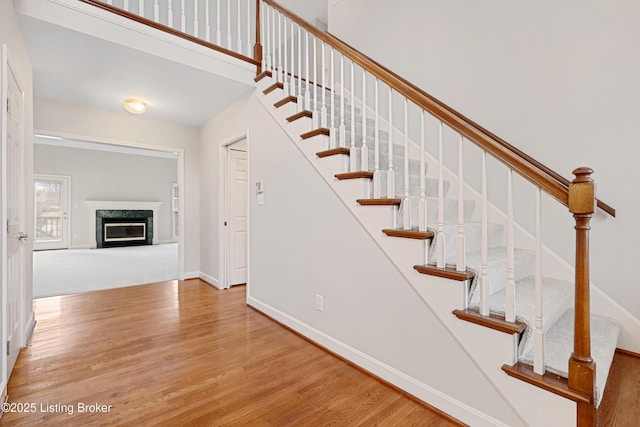 stairway with a fireplace, wood finished floors, a towering ceiling, and baseboards